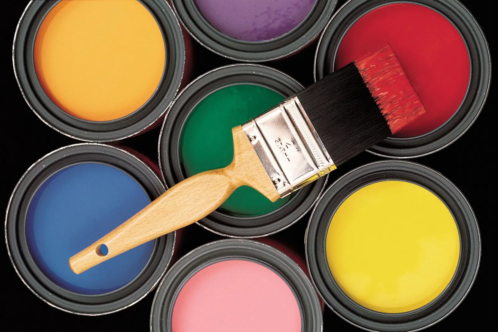 Paintbrush over open cans of colorful paint